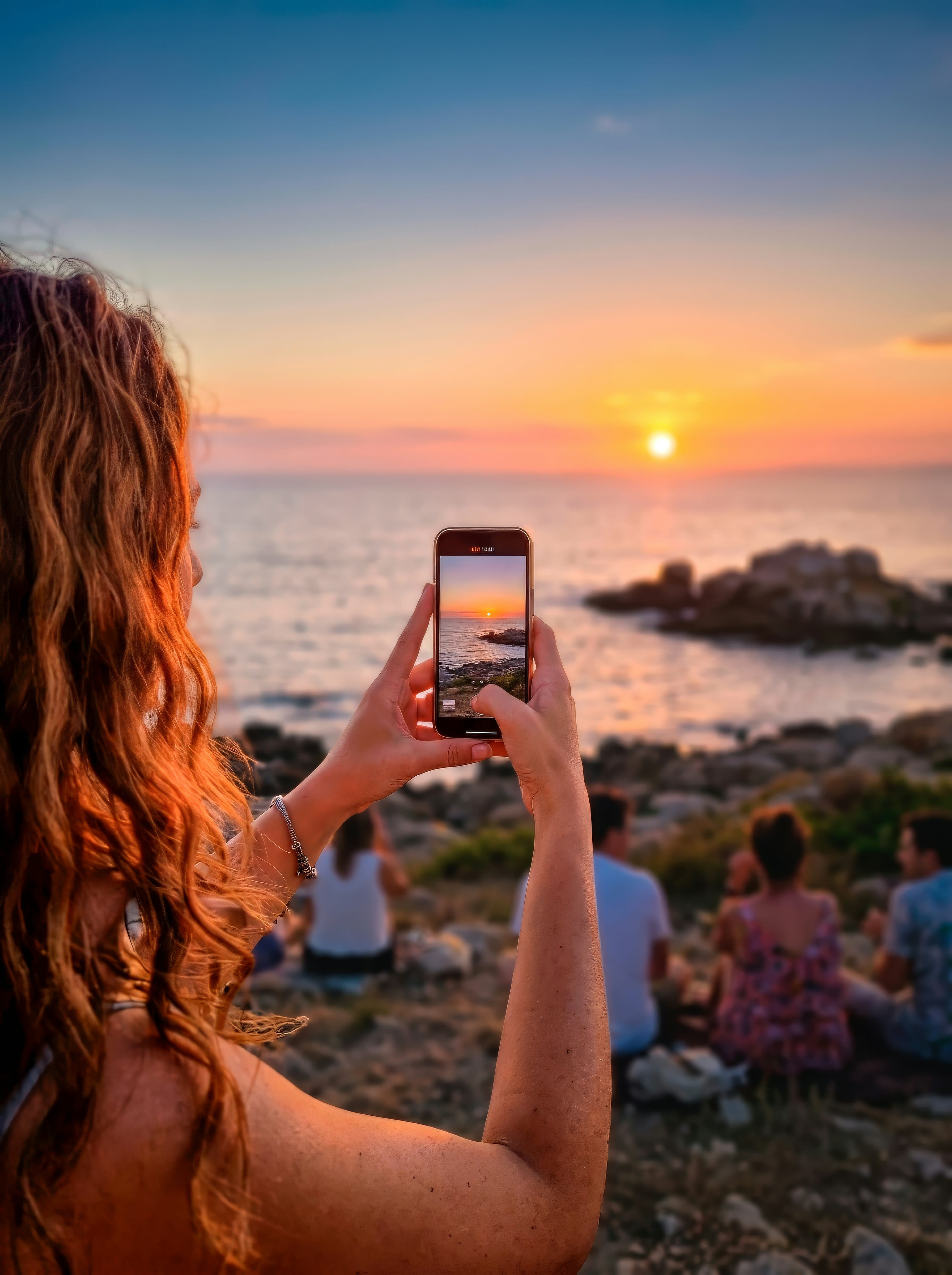 A woman capturing a golden sunset on her phone with friends