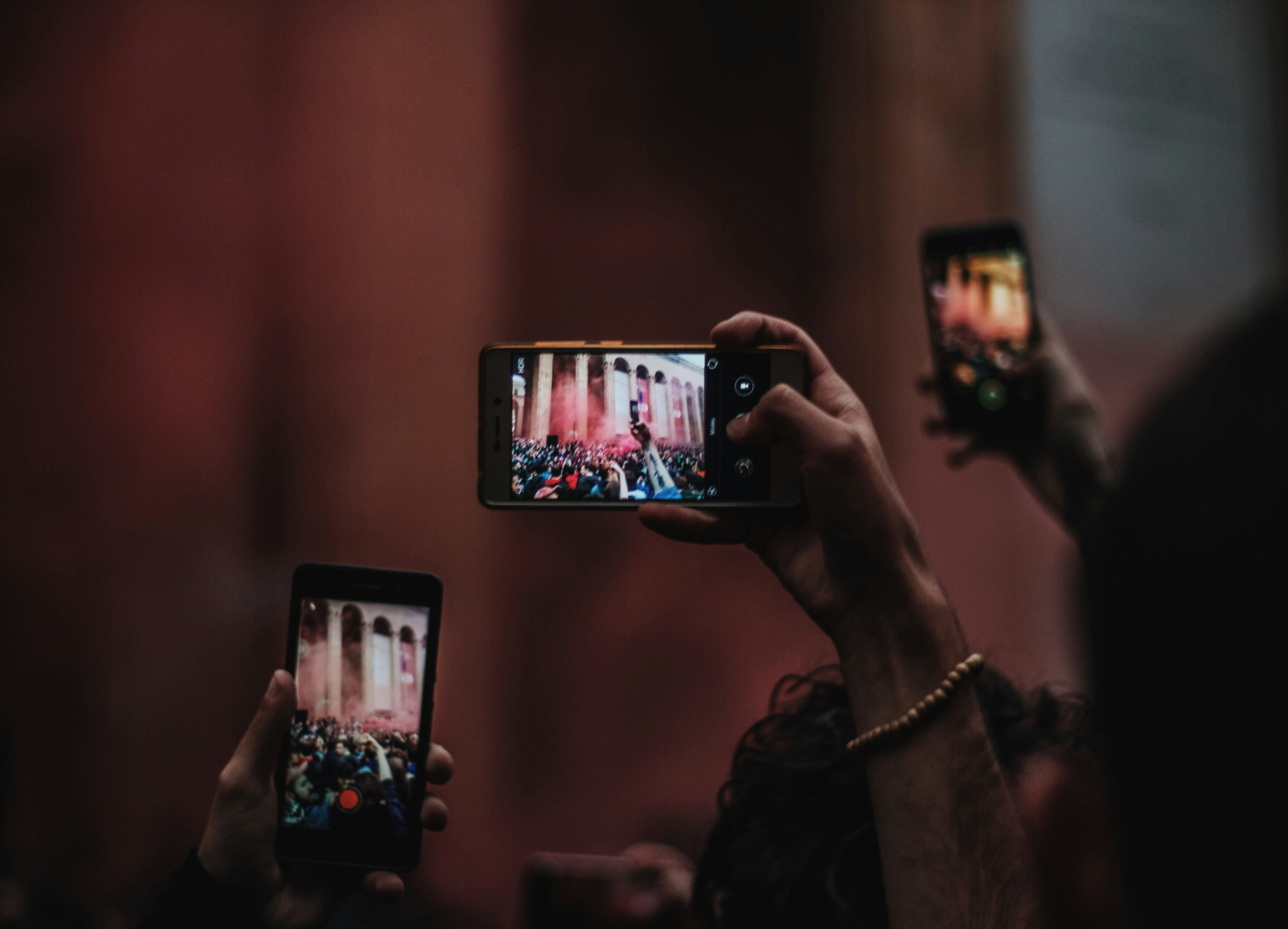 Hands holding up a phone to film a live concert with stage lights