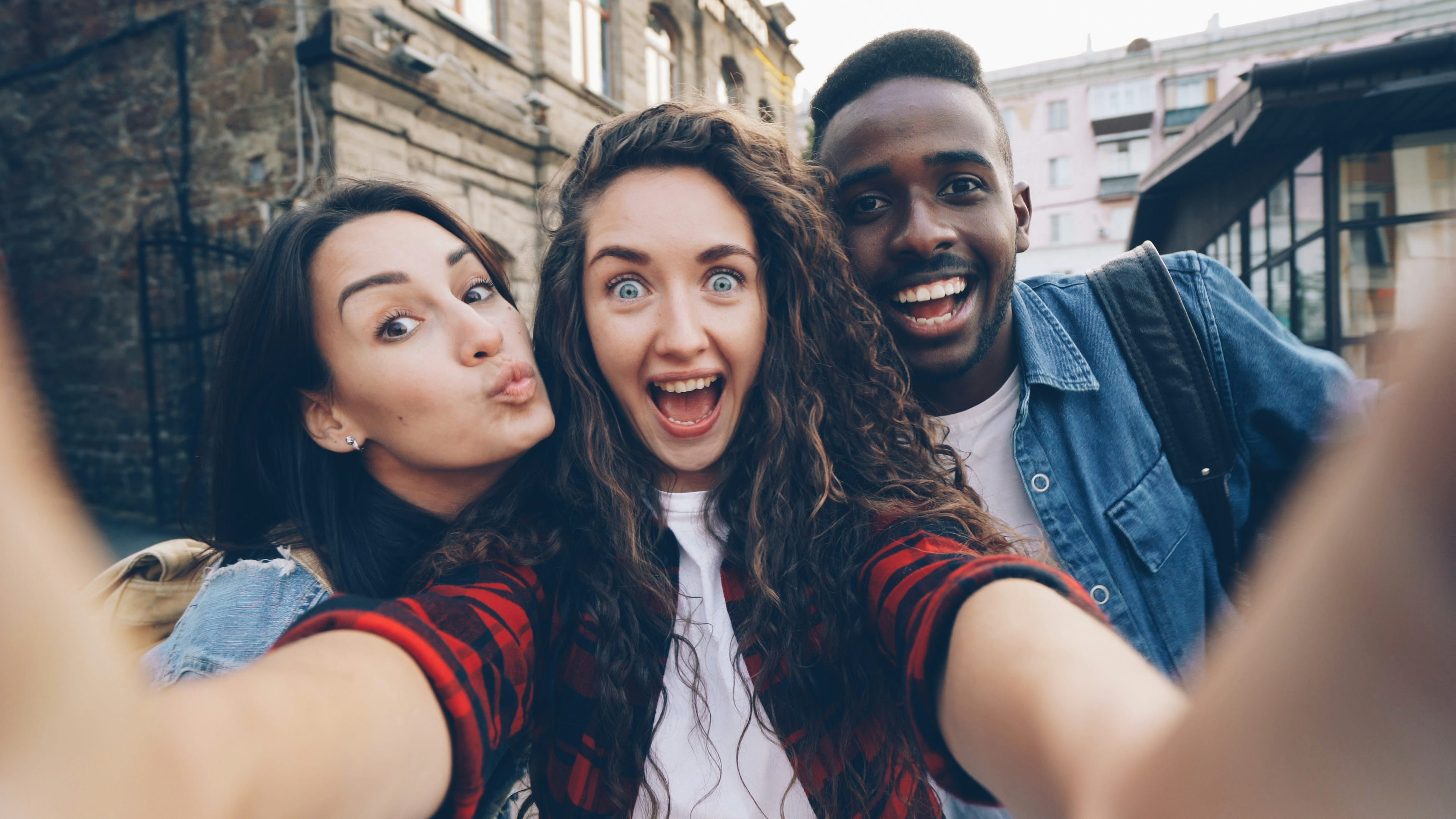 Three friends laughing together while taking a group selfie
