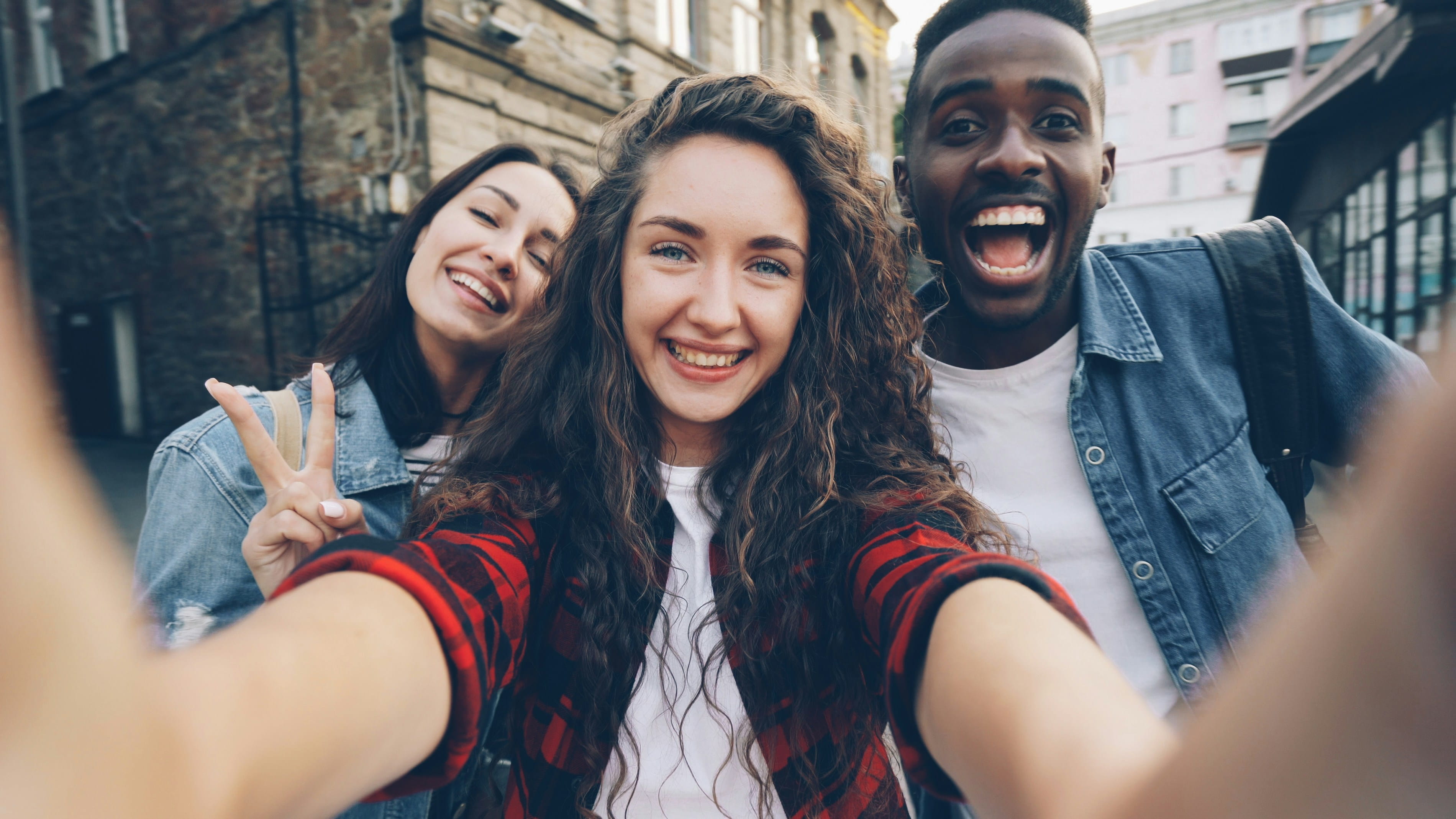 Three friends laughing together while taking a selfie in the city