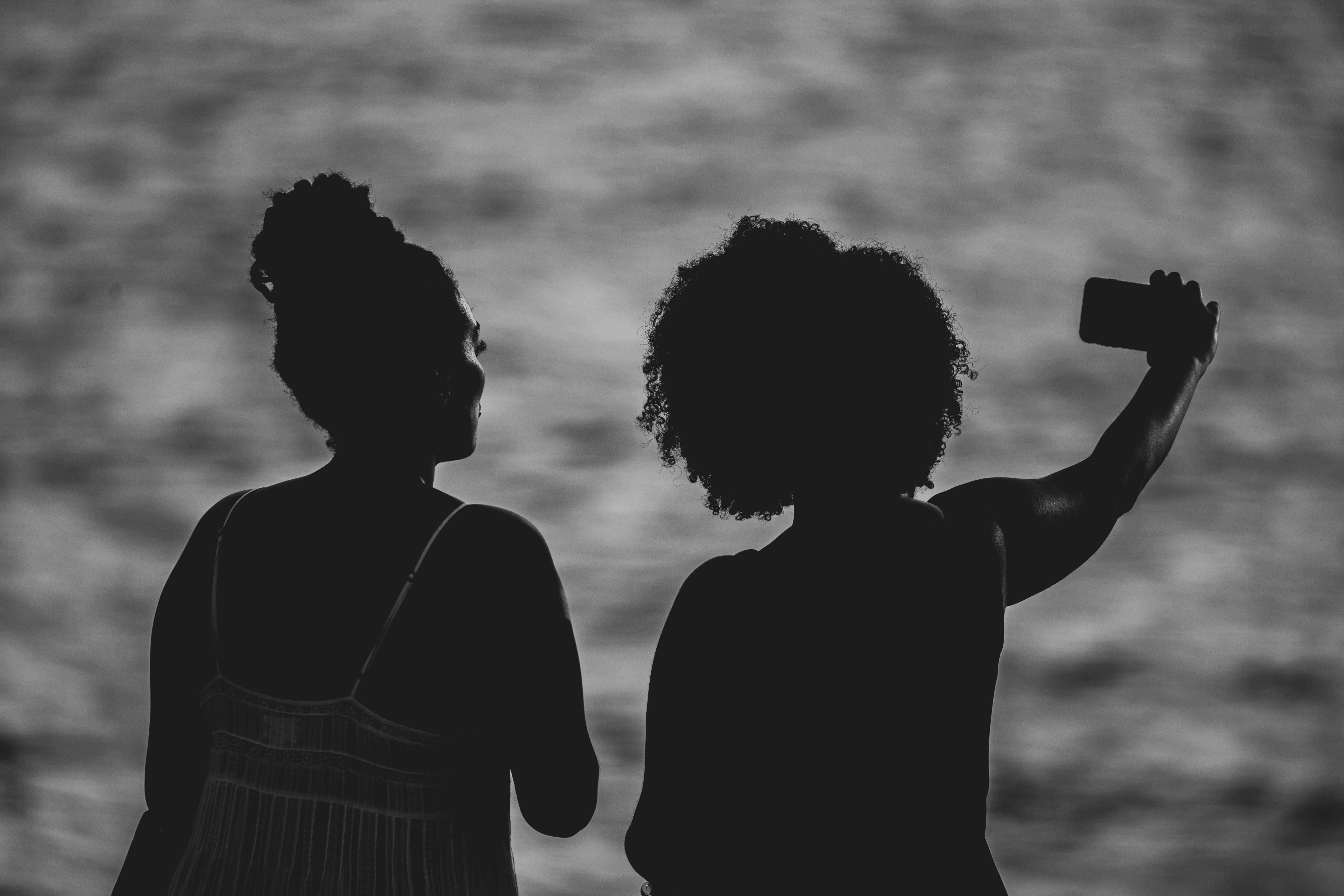 Two friends silhouetted against the water, taking a photo together